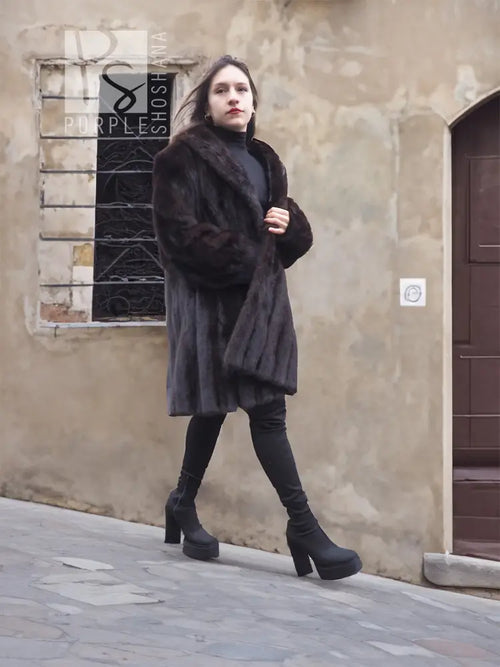 Dark hooded mink fur jacket coat, front view, hand near chest, long silhouette.