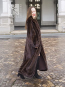 Long dark brown mink fur coat with open front and long hem, walking pose