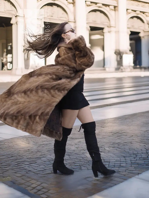Long mink section coat in brown with swing hem and button front; side view