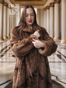 Long mink fur coat with plush texture in espresso brown, shown with clasped button at chest.