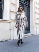 Hooded long mink fur coat with cross-stripe pattern, front view near doorway.