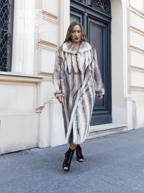 Hooded long mink fur coat with cross-stripe pattern, front view near doorway.