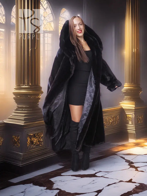 Black long hooded fur coat with open front and broad sleeves, styled over a short black dress