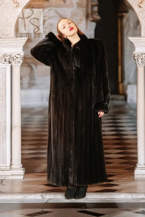 Long black mink coat with high collar and button placket, model in front view.
