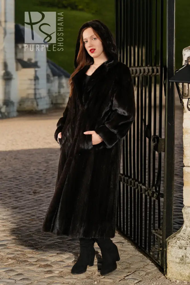 Black hooded mink coat, buttonless open front; model standing near doorway.