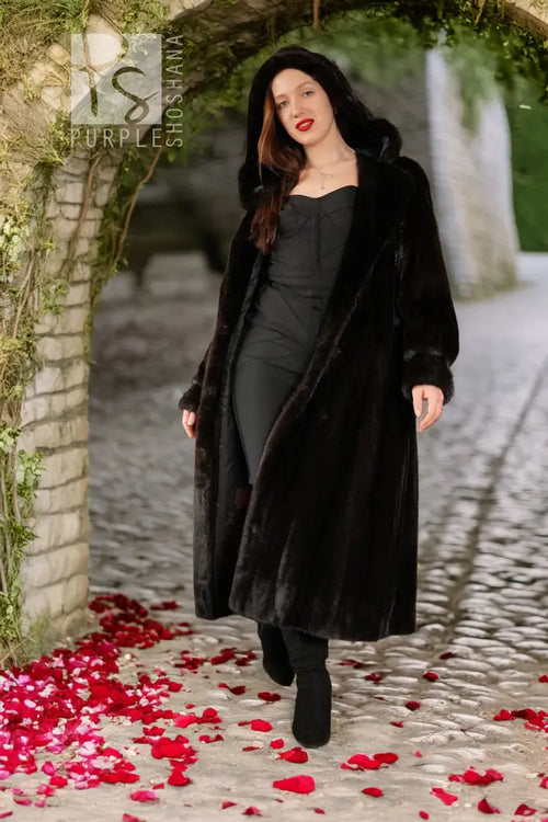 Black hooded mink coat with long hem and soft drape; model walking, hood up.