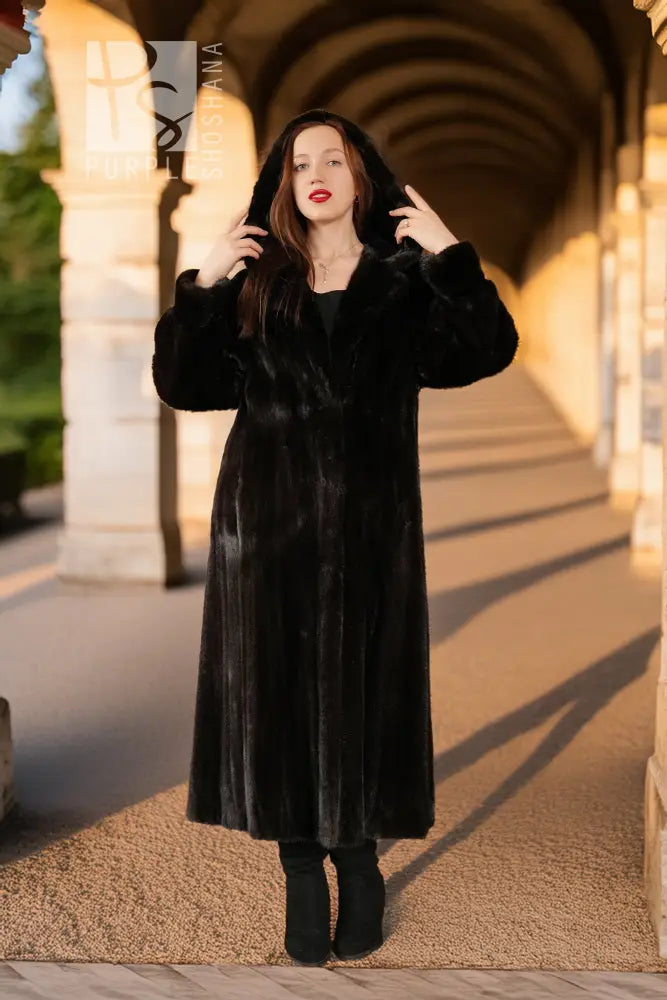 Black hooded mink coat, full length; model wearing hood and posing with both hands up.