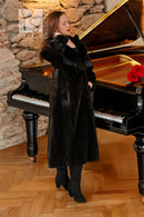 Black hooded mink coat standing near piano, long length, wide sleeves