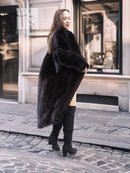 Black mink fur long coat with high collar and asymmetrical front flare, walking stance.