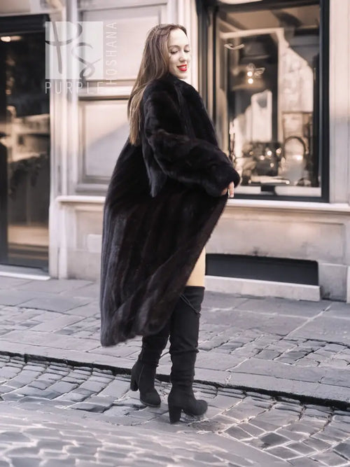Black mink fur long coat with high collar and asymmetrical front flare, walking stance.
