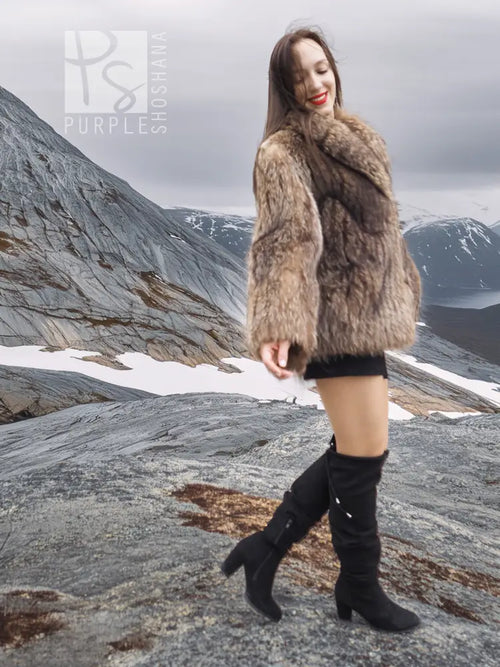 Brown faux-fur jacket with high collar and long sleeves, model standing on rocky ground.