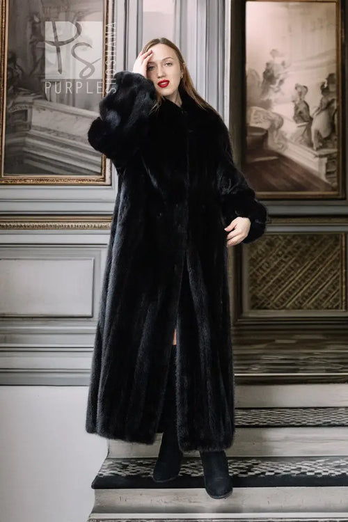 Black mink full-length coat with high collar and button front; sleeve and front slit visible.