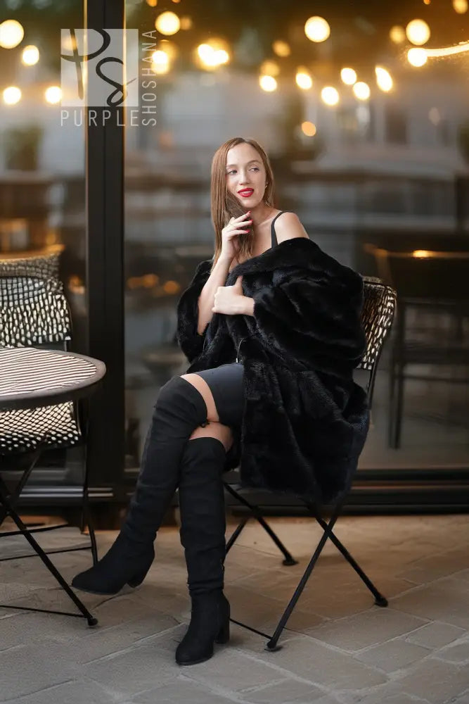 Black hooded mink coat with open front and voluminous hood, worn with fitted outfit.