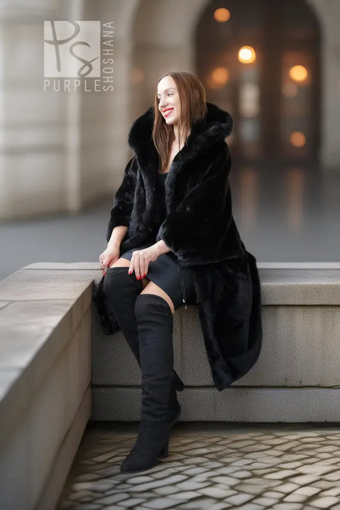 Black hooded mink coat with open front and voluminous hood, paired with knee-high boots.
