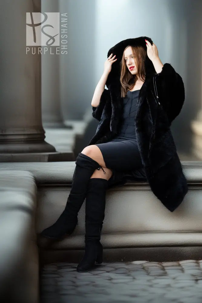 Black hooded mink coat with soft fur texture, open front, worn with tall black boots.