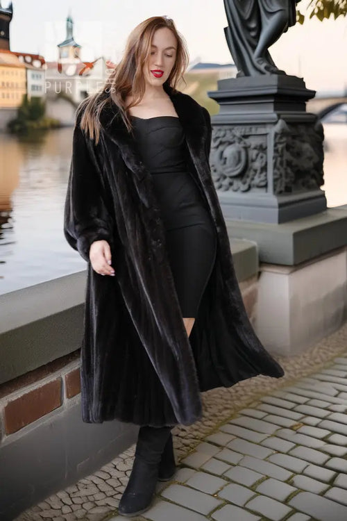 Black mink coat with long hem and wide sleeves, worn over a fitted black dress.