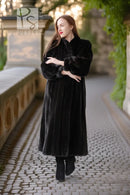 Black fur coat with button-front, long sleeves, mid-calf length, hands crossed.
