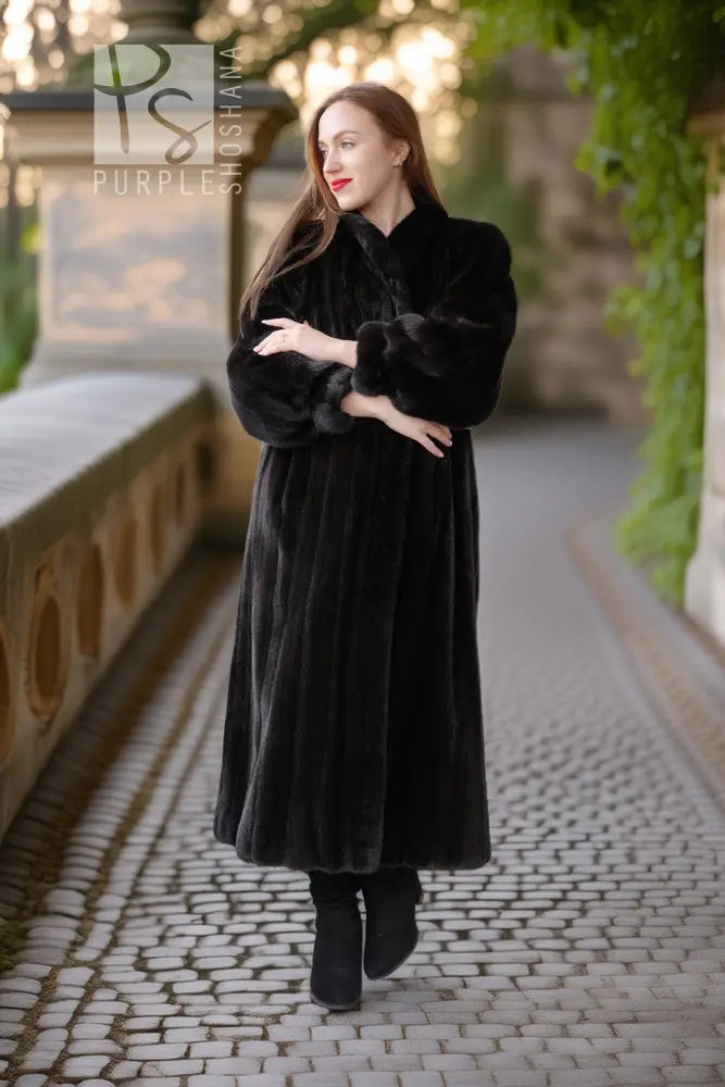 Black fur coat with button-front, long sleeves, mid-calf length, hands crossed.