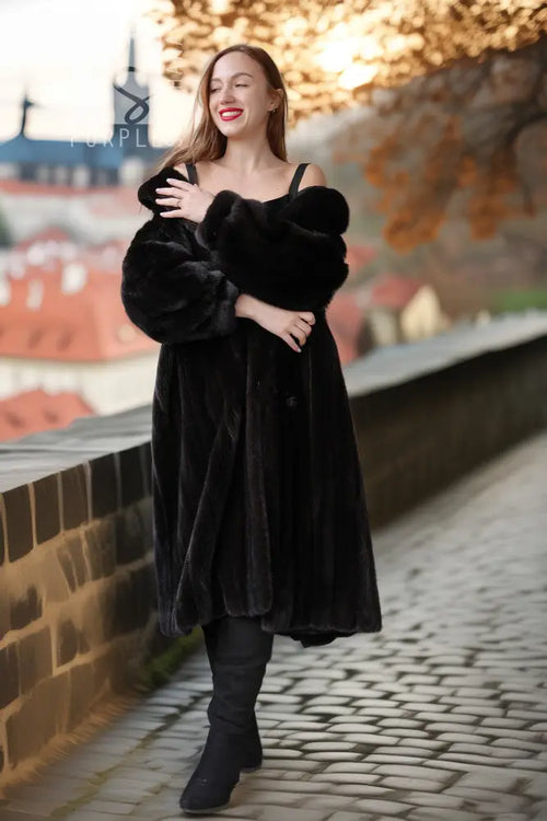 Black mink coat with wide sleeves and button front, styled with dark knee-high boots.