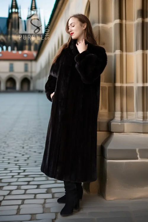 Black fur coat with button-front, long sleeves, mid-calf length, standing near steps.