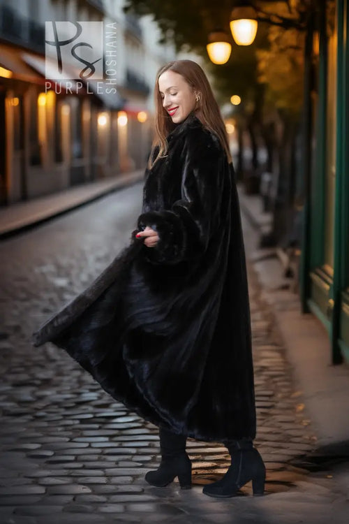 Black mink fur full-length coat with button front and high collar, walking pose on cobblestones.