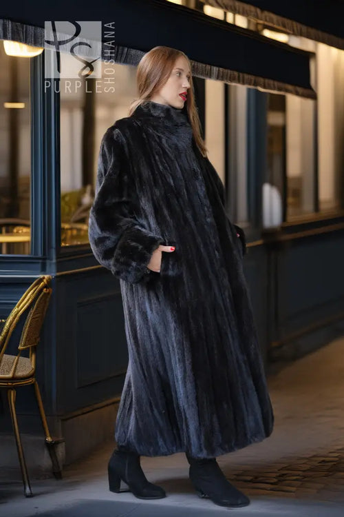 Black mink fur long coat with textured fur sleeves and high collar, side view outdoors.