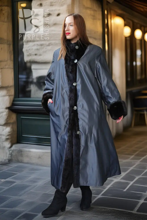 Black mink fur long coat with high collar and button closure, standing in front of shop door.
