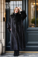 Black mink fur long coat with stand collar and button placket, full body view outdoors.
