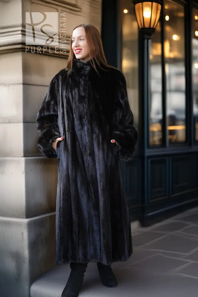 Black mink fur long coat with high collar and button front, front view near building entrance.