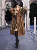 Women's brown mink fur coat with plush collar, hands up styling, knee-length.