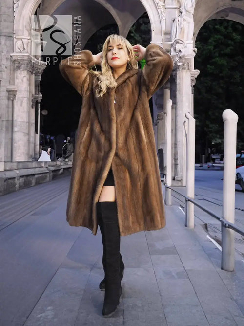 Women's brown mink fur coat with plush collar, hands up styling, knee-length.