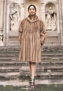 Light brown mink fur coat with hood, full front view standing outdoors.