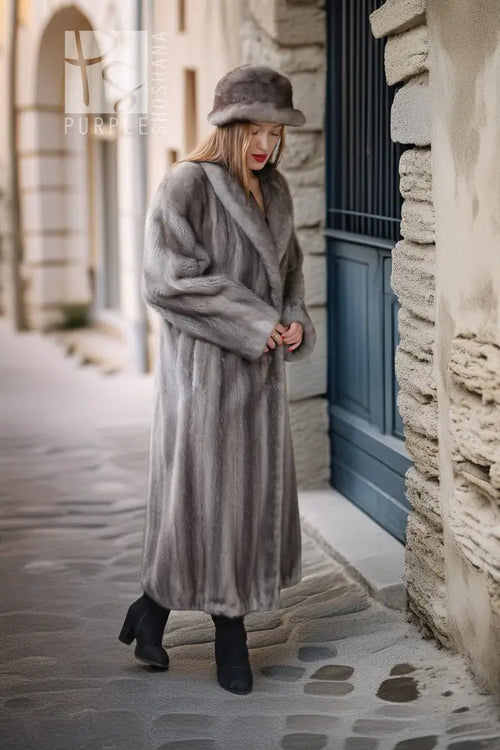 A woman wearing a long gray fur coat, matching fur hat, and black ankle boots stands on a cobblestone street in front of a stone building with a blue door.