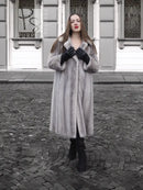 Grey mink fur coat with hood and buttoned front, black leather-style gloves.