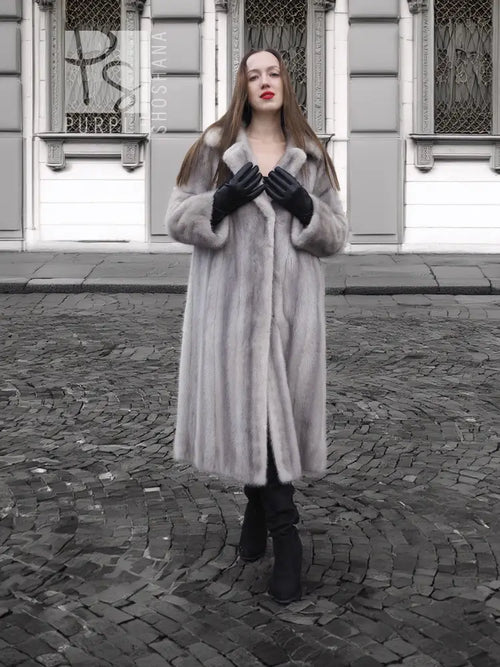 Grey mink fur coat with hood and buttoned front, black leather-style gloves.