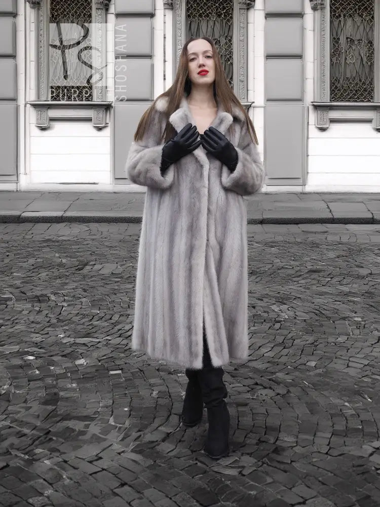 Grey mink fur coat with hood and buttoned front, black leather-style gloves.
