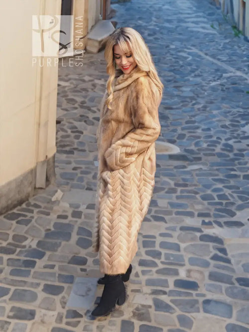 Long tan mink fur coat with hood and herringbone design along the sleeves and hem.