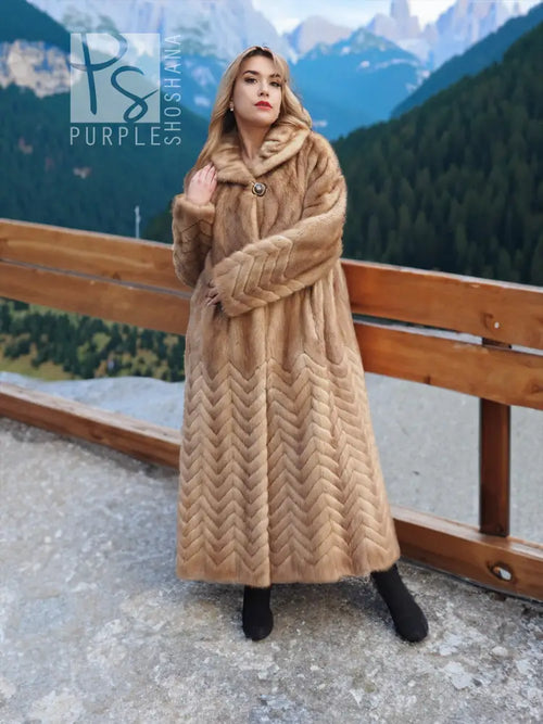 Long tan mink fur coat with hood, chevron/herringbone design and button-front fastening.