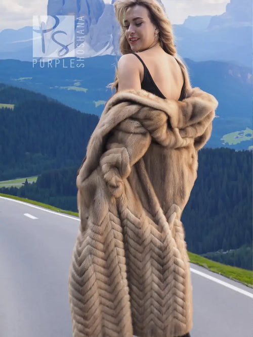 Tan mink fur hooded coat with herringbone pattern, worn over a dark sleeveless dress.