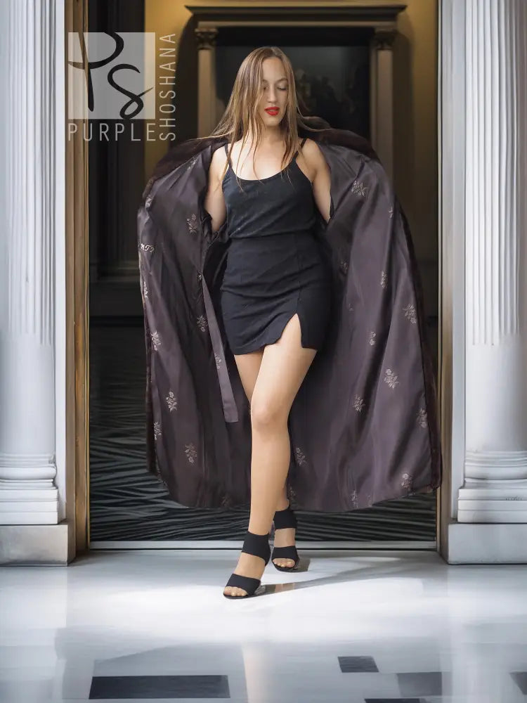 Long mahogany mink fur coat with wide sleeves, draped open over a black dress.