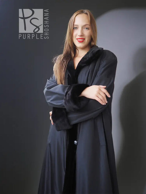 Reversible sheared mink coat in dark black with button-front and standing collar, arms crossed.