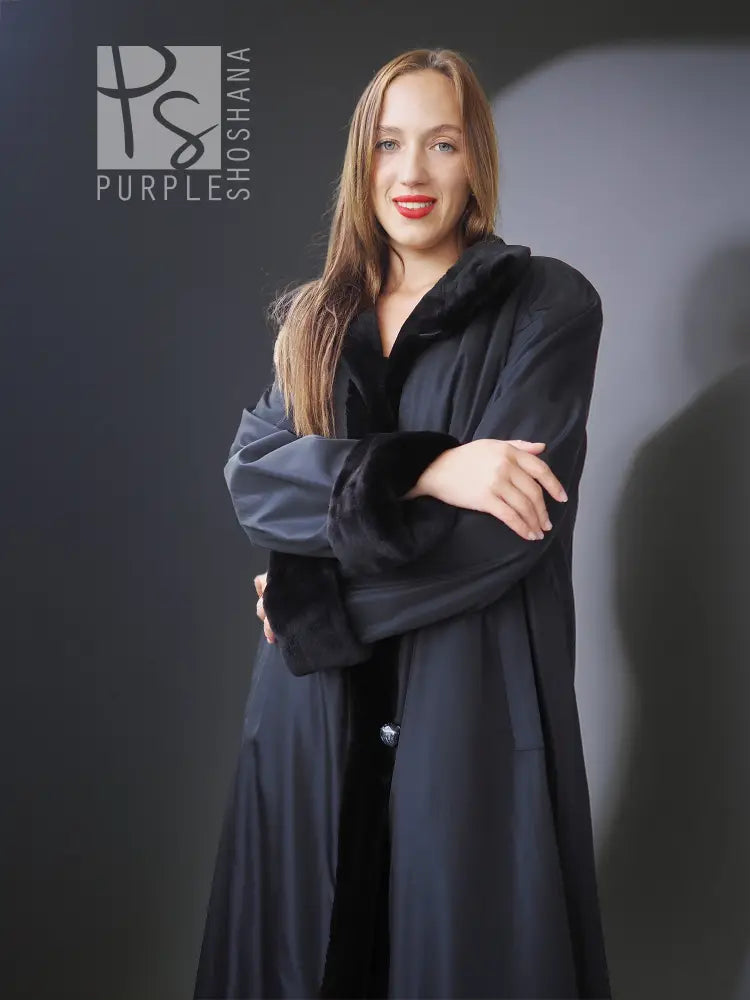 Reversible sheared mink coat in dark black with button-front and standing collar, arms crossed.