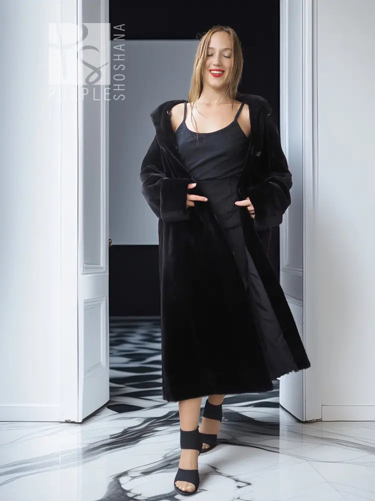 Black mink coat with button closure and wide sleeves, front slit and dark dress