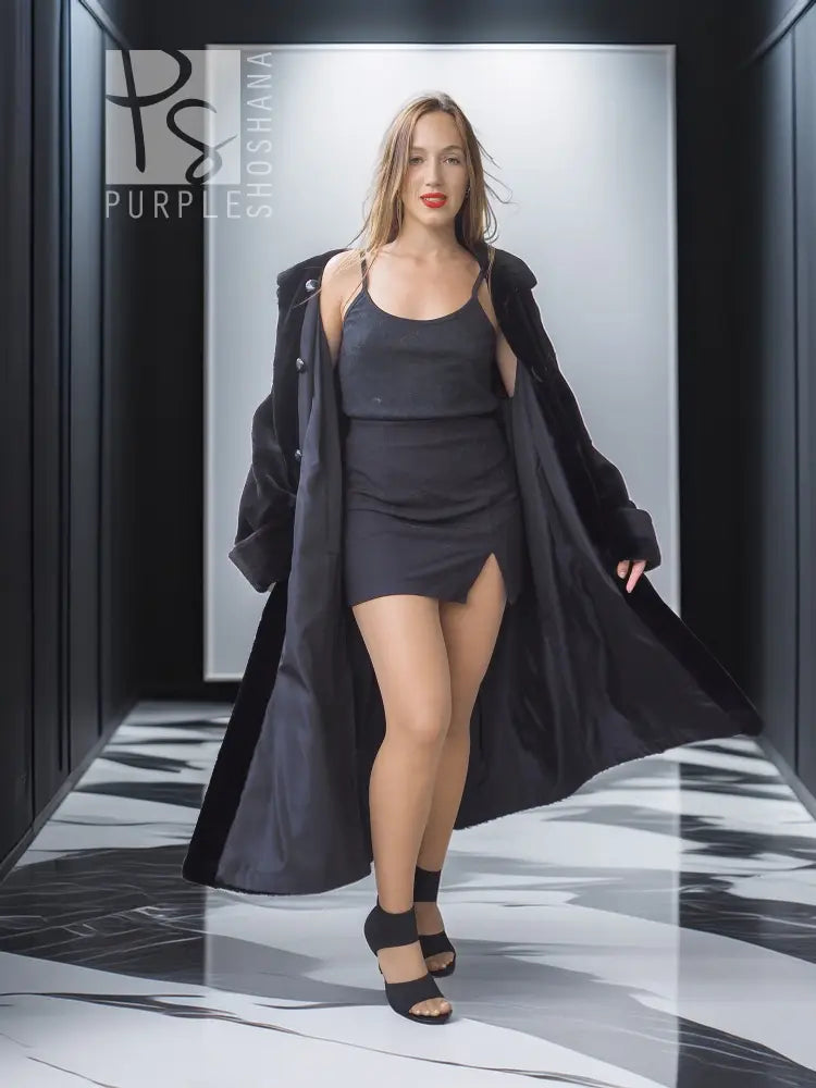 Long black mink coat worn open over a black dress, side slit visible