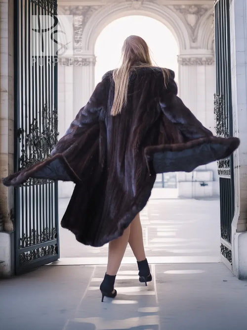 Black mink full-length coat, rear view with hooded collar and open side slit.