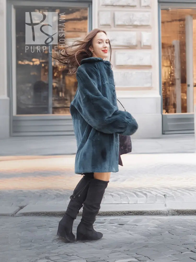 Deep teal sheared muskrat fur coat with long sleeves and flared hem, side walking view
