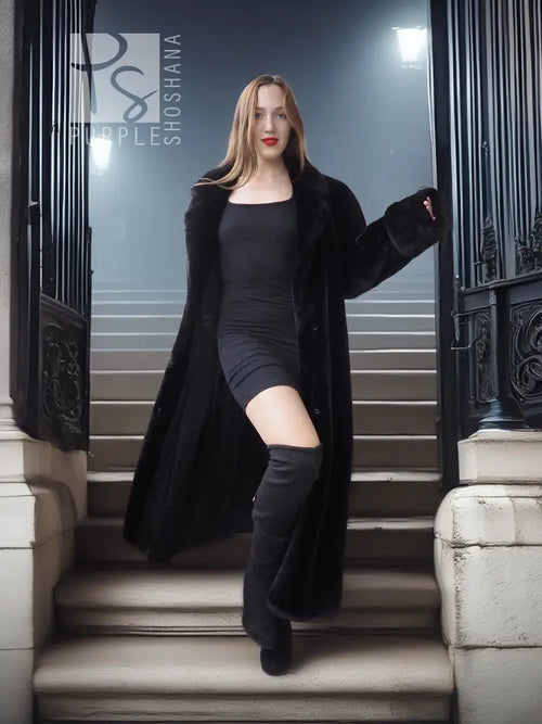 Long black fur coat worn over a fitted black dress, open front