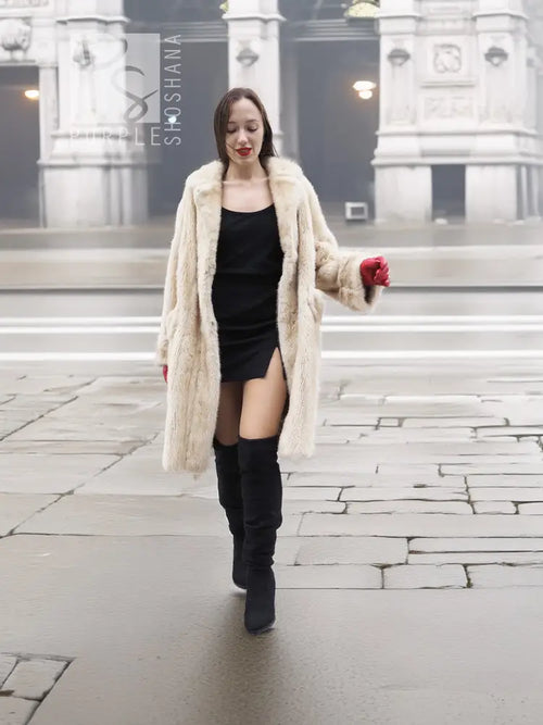 Beige mink fur coat with open front and long sleeves, worn with red gloves