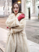 Beige mink fur coat close-up with open neckline and textured fur, held by red gloves