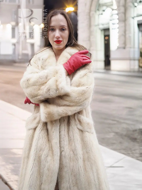 Beige mink fur coat close-up with open neckline and textured fur, held by red gloves